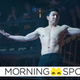 A shirtless Shang-Chi (Simu Liu) raises his arms in front of a crowd of cage match fans.
